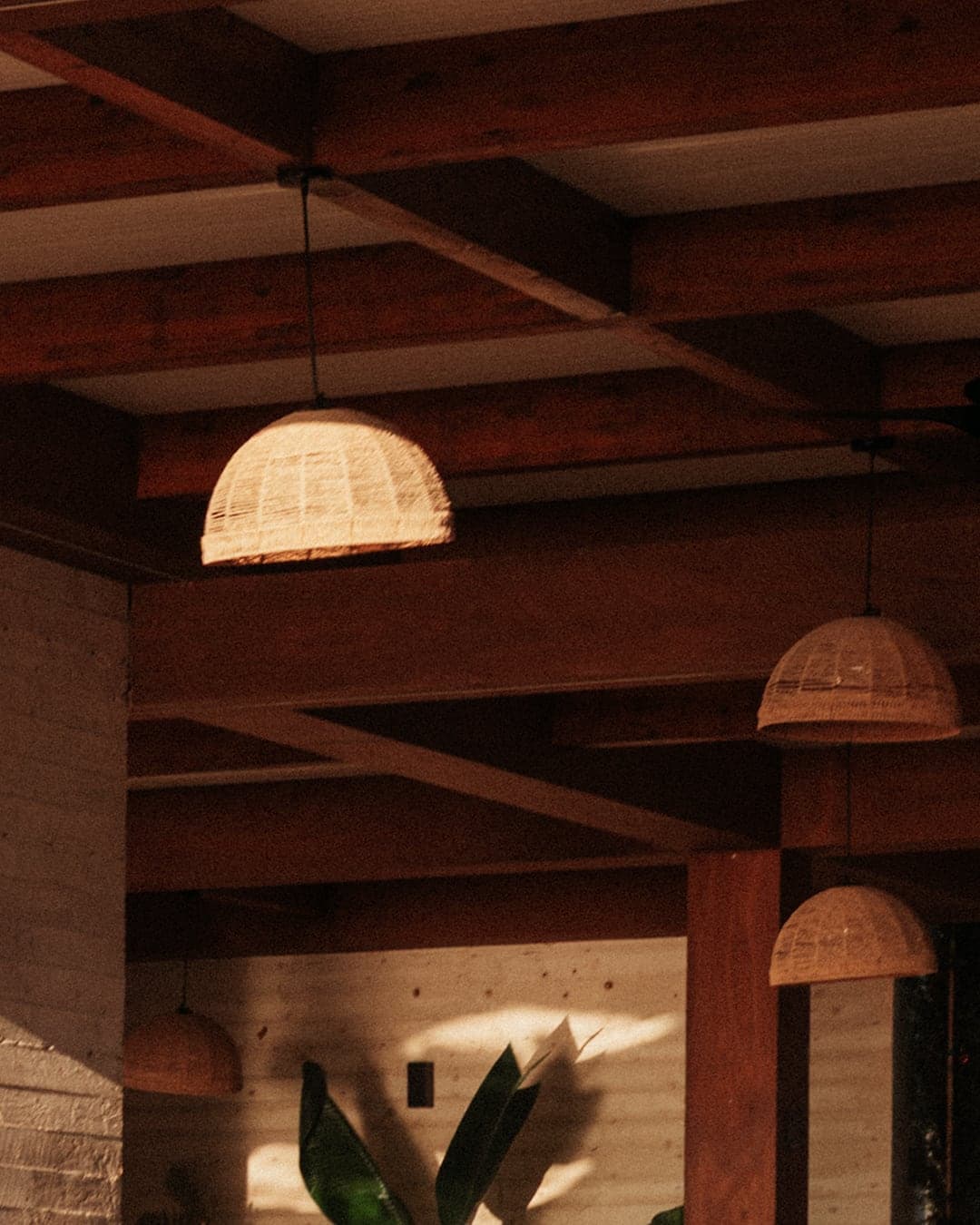 Rattan pendant lamps glowing beneath dark stained timber beams - the warmest, darkest corner of the lounge.